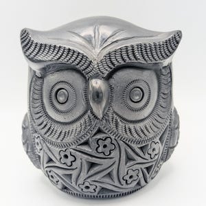 Puede incluir: Una figurita de búho de cerámica negra con detalles intrincados. El búho tiene ojos grandes y un patrón detallado de flores y hojas en su cuerpo.