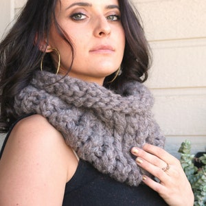 May include: A gray knitted cowl neck scarf with a chunky knit texture.