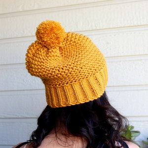 May include: A mustard yellow knitted beanie with a fluffy pom pom on top.