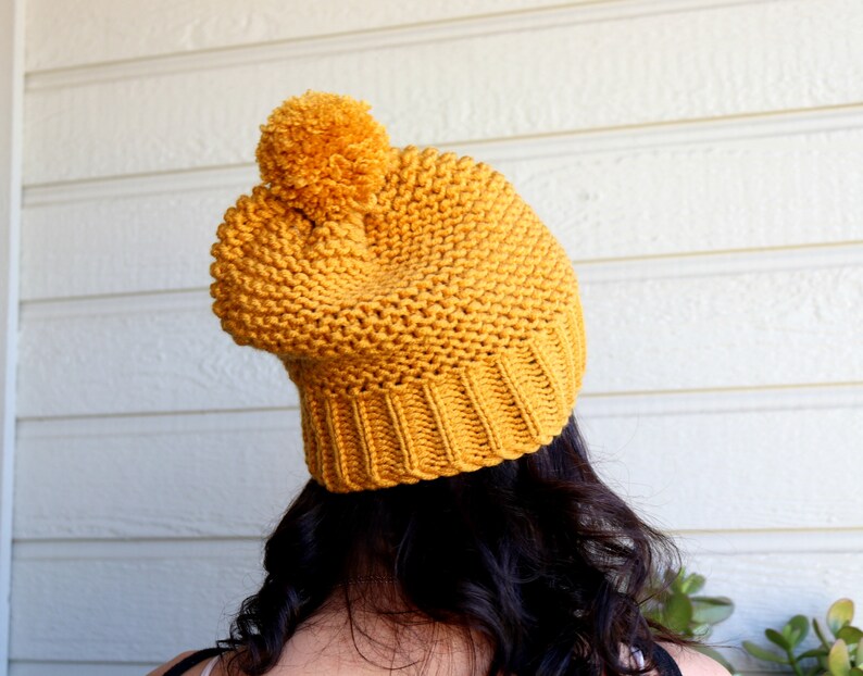 May include: A mustard yellow knitted beanie with a fluffy pom pom on top.