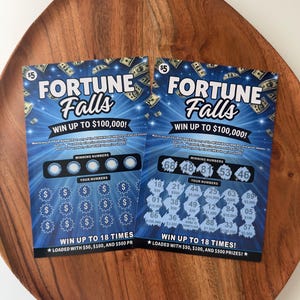 May include: Two Fortune Falls scratch-off lottery tickets with blue backgrounds, white text, and dollar sign graphics. One ticket is unscratched, while the other shows revealed numbers and prize amounts, including the text We're Going To Disneyland.