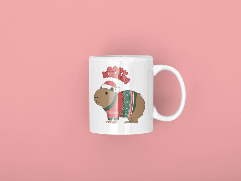 Pu&ograve; includere: Tazza in ceramica bianca con un capibara dei cartoni animati che indossa un cappello da Babbo Natale e un maglione festivo con motivi rossi, verdi e bianchi. La tazza ha le parole "Happy Xmas" sopra il capibara. Lo sfondo &egrave; rosa.