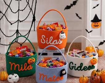 May include: Four round woven rope baskets in orange, green, light blue, and white, each featuring a handle and a personalized name in script font. The baskets are filled with assorted candy and decorated with small felt Halloween-themed icons.