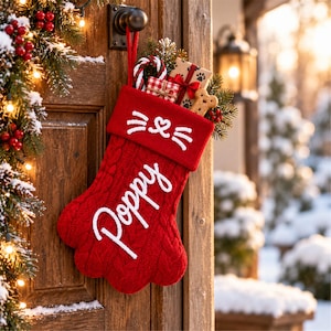 Peut inclure: Une chaussette de Noël rouge en tricot torsadé en forme de patte, avec le nom Poppy brodé en écriture blanche. Le revers présente un motif brodé blanc de nez et de moustaches de chat, rempli d'un sucre d'orge et de petits cadeaux.