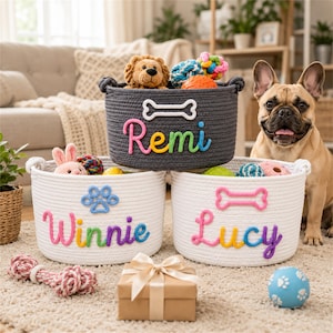 May include: Three round woven rope storage baskets, one dark gray and two white, featuring colorful rope lettering and shapes. The dark gray basket displays the name Remi with a bone, while the white baskets show the names Winnie with a paw print and Lucy with a bone. Various plush pet toys are inside the baskets.