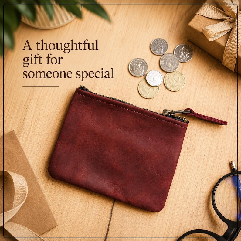 Pu&ograve; includere: Un portamonete in pelle bordeaux con cerniera nera e una piccola linguetta. Il testo "Un regalo premuroso per una persona speciale" &egrave; visualizzato. Sono visibili anche diverse monete e una piccola confezione regalo con un nastro.