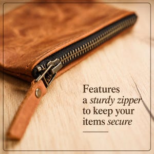 Pu&ograve; includere: Primo piano di una custodia in pelle marrone con una robusta cerniera nera e un tirazip in metallo. Il testo sull'immagine recita: "Features a sturdy zipper to keep your items secure."