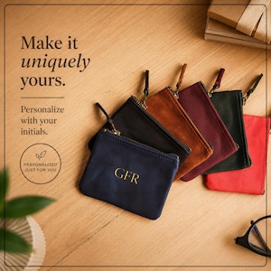 Pu&ograve; includere: Una collezione di portamonete in pelle personalizzate in vari colori, tra cui blu navy, nero, marrone, bordeaux, verde scuro e rosso. Ogni portamonete presenta una chiusura con cerniera e iniziali dorate. Il testo "Make it uniquely yours" &egrave; visibile.