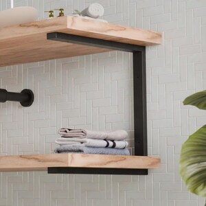 Könnte beinhalten: Ein modernes Badezimmer-Waschtisch mit einem hellen Holzregal und schwarzen Metallstützen. Der Waschtisch umfasst ein Waschbecken, einen Wasserhahn und ein schwarzes Rohr. Dekorative Pflanzen und Handtücher sind ebenfalls sichtbar.