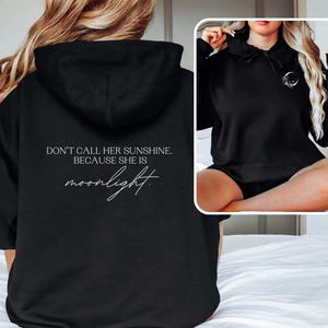 K&ouml;nnte beinhalten: Schwarzer Kapuzenpullover mit dem wei&szlig;en Schriftzug "DON'T CALL HER SUNSHINE. BECAUSE SHE IS moonlight.". Der Hoodie hat eine Kapuze und eine kleine Mondgrafik. Das Bild zeigt die R&uuml;ckseite und ein kleineres Vorschaubild.