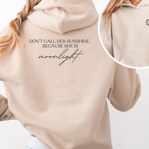 K&ouml;nnte beinhalten: Beigefarbener Kapuzenpullover mit dem Text "DON'T CALL HER SUNSHINE. BECAUSE SHE IS moonlight." auf dem R&uuml;cken. Auf der Vorderseite befindet sich eine kleine Grafik eines Halbmonds mit floralen Akzenten. Der Hoodie hat eine Kapuze und eine Vordertasche.