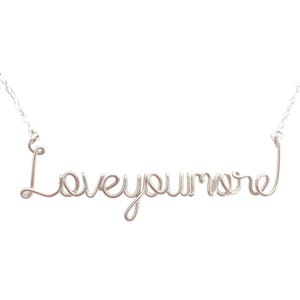 May include: A silver-colored wire necklace spelling out "Loveyoumore" in cursive script. The necklace hangs from a delicate chain, with the word's letters connected. The background is plain white.