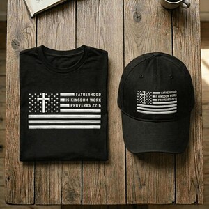 May include: Black t-shirt and baseball cap with a white and black flag design. The flag design includes a cross and the text "FATHERHOOD IS KINGDOM WORK PROVERBS 22:6". The cap is a standard baseball style.