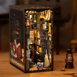 May include: A white ceramic mug with a black handle and the text "But First, Coffee" in a black, handwritten-style font. The mug is on a white surface.