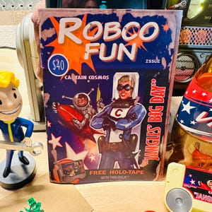 Könnte beinhalten: Ein Comic-Cover im Retro-Stil mit dem Titel "ROBCO FUN" und einem Weltraumthema. Das Cover zeigt Captain Cosmos und einen Weltraumaffen mit dem Text "JANGLES BIG DAY" und "FREE HOLO-TAPE".