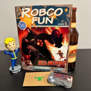 May include: A collection of Fallout-themed merchandise. Includes a "Robco Fun" comic book, a Vault-Tec figurine, a bottle of Sarsaparilla, a cassette player, and a small green creature. The comic book features the text "Red Menace".