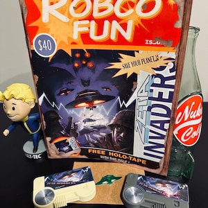 May include: A collection of Fallout-themed merchandise. Includes a "Robco Fun" sign, a Vault Boy figurine, a Nuka-Cola bottle, and two "Zeta Invaders" game cartridges. The sign features retro sci-fi artwork and the text "Save Your Planet!!"