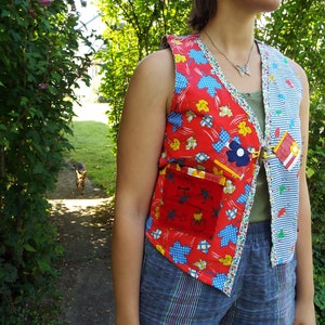 May include: A red and blue patchwork vest with a floral print and a large pocket on the front. The vest has a button closure and is made of a variety of fabrics.