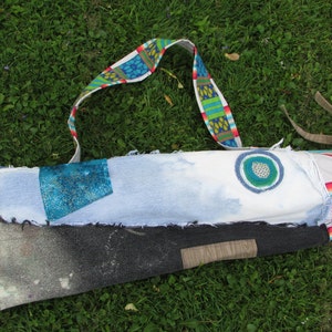 May include: A blue and white yoga mat bag with a colorful strap. The bag is made of recycled denim and has a circular design on the front.