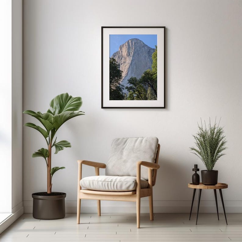 Puede incluir: Una fotograf&iacute;a enmarcada de Half Dome, un acantilado de granito en el Parque Nacional de Yosemite, California. La fotograf&iacute;a est&aacute; colgada en una pared blanca sobre un sill&oacute;n de madera clara y una peque&ntilde;a mesa auxiliar con una planta en maceta.