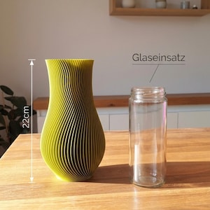 May include: A lime green vase with a vertical ribbed texture and a height of 22 cm, accompanied by a clear glass insert labeled Glaseinsatz. The vase has a curved, tapered silhouette and a wide opening at the top, designed to hold the glass cylinder.