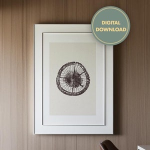 May include: A white framed print of a tree trunk cross-section with a brown and white design hangs on a wood-paneled wall. A brown leather office chair sits in front of a white desk with a black lamp.