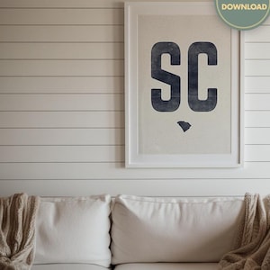 Può includere: Una stampa incorniciata bianca con le lettere "SC" in blu su uno sfondo bianco. La stampa è appesa a una parete di legno bianca. Le lettere sono in un carattere grassetto e a blocchi.