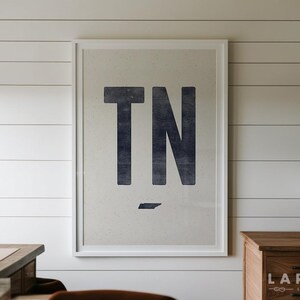 Pu&ograve; includere: Una stampa artistica incorniciata con le grandi lettere blu navy scuro TN centrate su uno sfondo color crema chiaro con una sottile trama punteggiata. Sotto le lettere si trova una piccola silhouette blu navy a tinta unita dello stato del Tennessee.