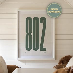 May include: A framed print featuring the number "802" in a bold, rounded font, in a muted green color. The print is set against a white background and framed in a white border. A "Digital Download" sticker is in the upper right corner.