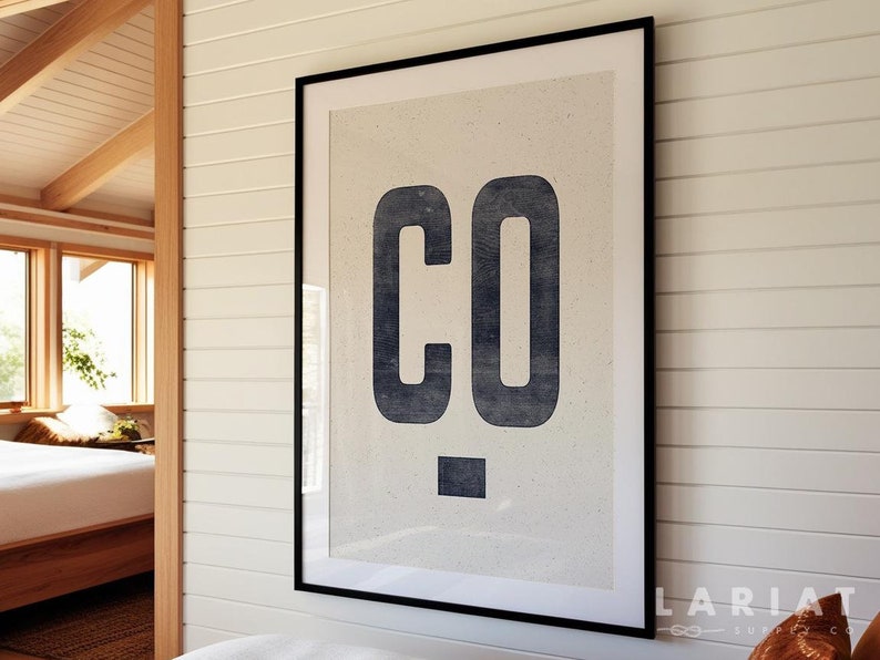 Puede incluir: Un estampado enmarcado con las letras "CO" en azul oscuro sobre un fondo beige claro. La obra de arte est&aacute; en un marco negro y cuelga de una pared blanca. El estampado tiene un dise&ntilde;o minimalista.