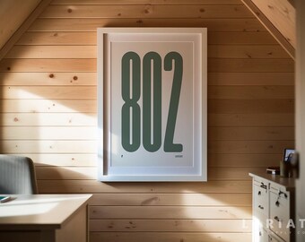 May include: A framed print with the number "802" in a bold, green font against a white background. The artwork is displayed on a light wood-paneled wall, creating a minimalist aesthetic. The print is in a white frame.