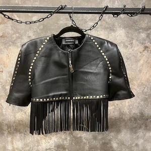 Op de afbeelding: Een zwart leren jack met gouden studs en franjes. Het jack heeft een ritssluiting en korte mouwen.