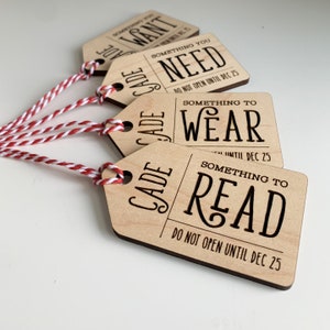 May include: Four wooden gift tags with red and white twine. The tags are engraved with the words "Something You Want", "Something You Need", "Something to Wear", and "Something to Read". Each tag also says "Do Not Open Until Dec 25".