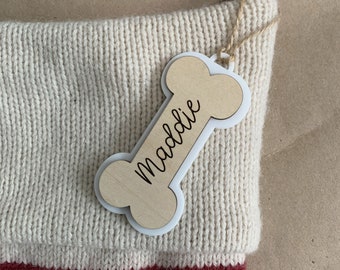 May include: A white knitted stocking with a red cuff and a wooden bone-shaped tag that says "Maddie".