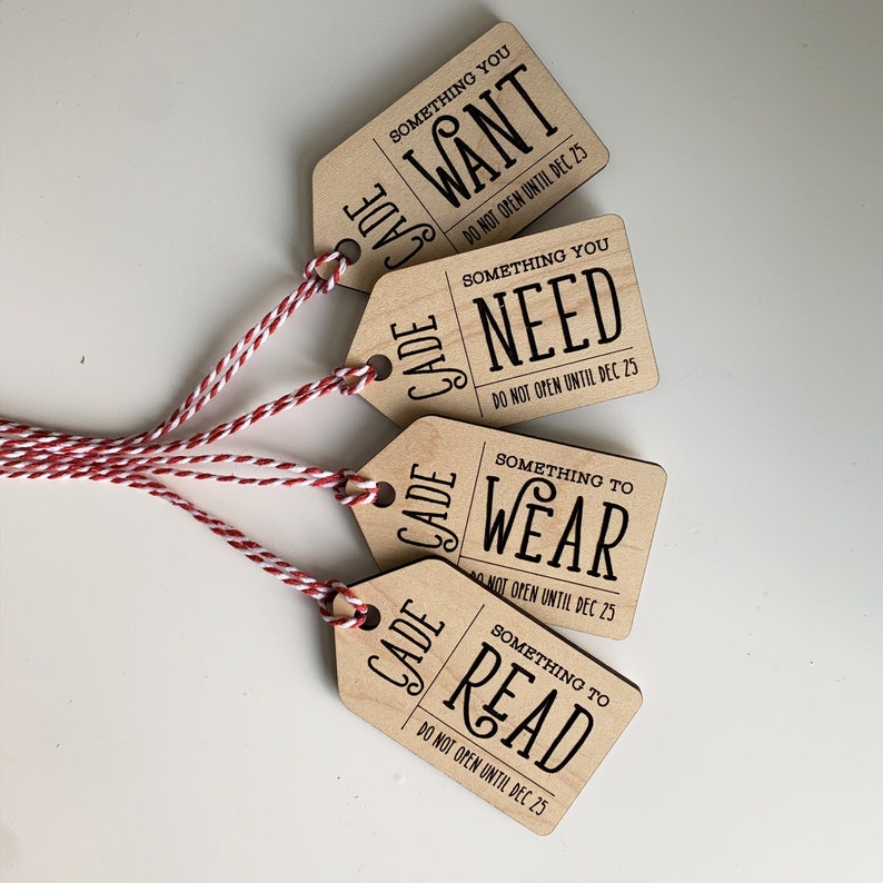May include: Four wooden gift tags with red and white twine. Each tag has a different message in black text: "Something You Want", "Something You Need", "Something to Wear", and "Something to Read". The tags also say "Do Not Open Until Dec 25".