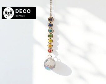 May include: A decorative hanging crystal suncatcher with a gold chain. The suncatcher features a series of colourful, round beads in a rainbow spectrum, topped with a clear, faceted crystal ball. The logo "DECO BYPRIVE" is in the upper left corner.