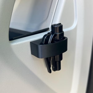 May include: A black plastic car door hook with a black tyre pressure gauge attached to it.