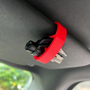 Può includere: Un clip per visiera da auto in plastica rossa con un multiutensile nero attaccato. Lo strumento ha una varietà di punte per diversi compiti.