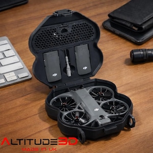 May include: Black drone carrying case with a gray drone inside. The case is open, revealing the drone, two batteries, and a screwdriver. The text "ALTITUDE 3D MADE IN UK" is printed in red and white.