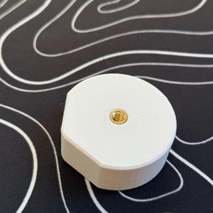 Może przedstawiać: Biały plastikowy adapter z gwintowanym otworem w kolorze złotym w środku.