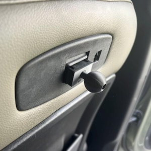May include: Close-up of a black plastic car seat adjustment lever with a round knob. The lever is attached to a beige car seat.