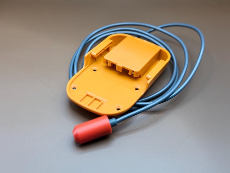 Op de afbeelding: Een gele plastic batterijlader met een blauwe kabel en een rode stekker.