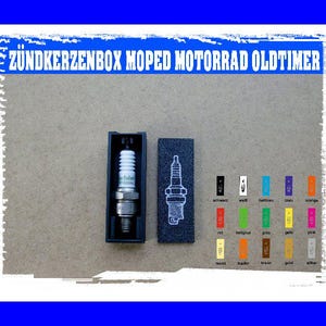 Può includere: Una candela in una scatola nera, con un'illustrazione corrispondente su un rettangolo blu scuro separato. L'immagine include il testo "ZÜNDKERZENBOX MOPED MOTORRAD OLDTIMER" in blu. È presente anche una tabella dei colori con varie etichette di colore.