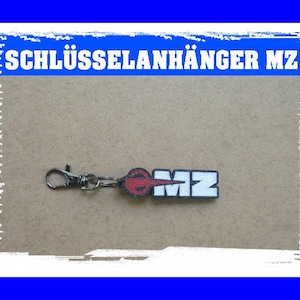 Könnte beinhalten: Ein Schlüsselanhänger mit dem Text "SCHLÜSSELANHÄNGER MZ" in weißen Buchstaben auf blauem Hintergrund. Der Schlüsselanhänger hat einen silbernen Verschluss und ein rechteckiges Etikett mit den Buchstaben "MZ" in Weiß, einem roten Design und einem schwarzen Rand.