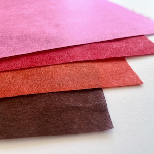 Puede incluir: Una pila de cuatro hojas rectangulares de fieltro dispuestas en un patrón en cascada. Los colores van desde un rosa brillante en la parte superior, seguido de un rojo vibrante, un naranja cálido y un marrón oscuro profundo en la base.