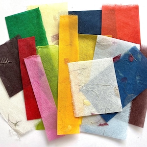 May include: A collection of rectangular and square sheets of handmade paper in various colors including red, yellow, green, blue, pink, white, and brown. Some sheets feature visible plant fibers and small embedded botanical elements throughout.