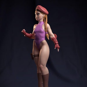 以下が含まれることがあります： 赤いベレー帽、ピンクのワンピース、茶色のブーツを履いた女性キャラクターのピンクと赤のアクションフィギュア。フィギュアは石の台座の上に立っています。
