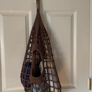 May include: A brown crocheted hanging storage bag with a white hook. The bag is filled with balls of yarn in various colors.