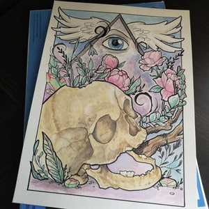 Peut inclure: Illustration à l'aquarelle représentant un crâne humain, des fleurs roses et un œil dans un triangle avec des ailes. L'œuvre utilise une palette de couleurs pastel avec des accents verts, roses et bleus. Le crâne est beige et l'œil est bleu.