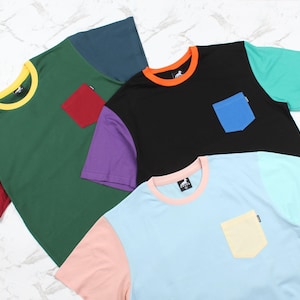 Puede incluir: Cuatro camisetas de diferentes colores con un bolsillo en cada una. Las camisetas son de color verde, negro, azul y rosa.